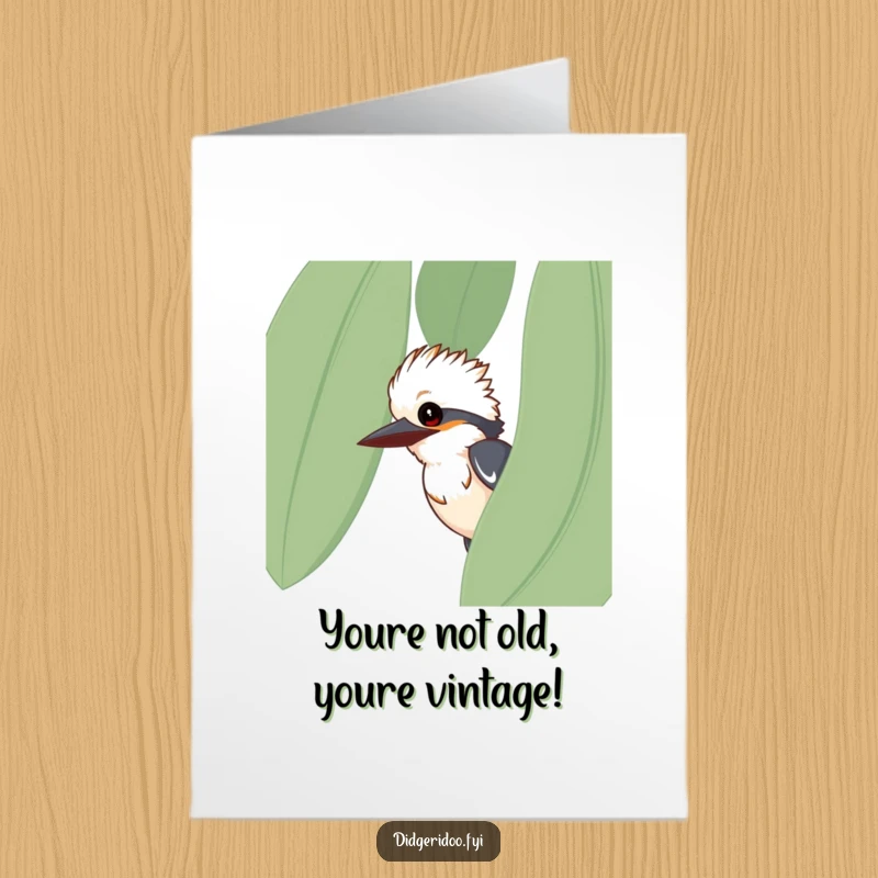 Funny free printable birthday card featuring a curious kookaburra peeking playfully from behind a large eucalyptus leaf.